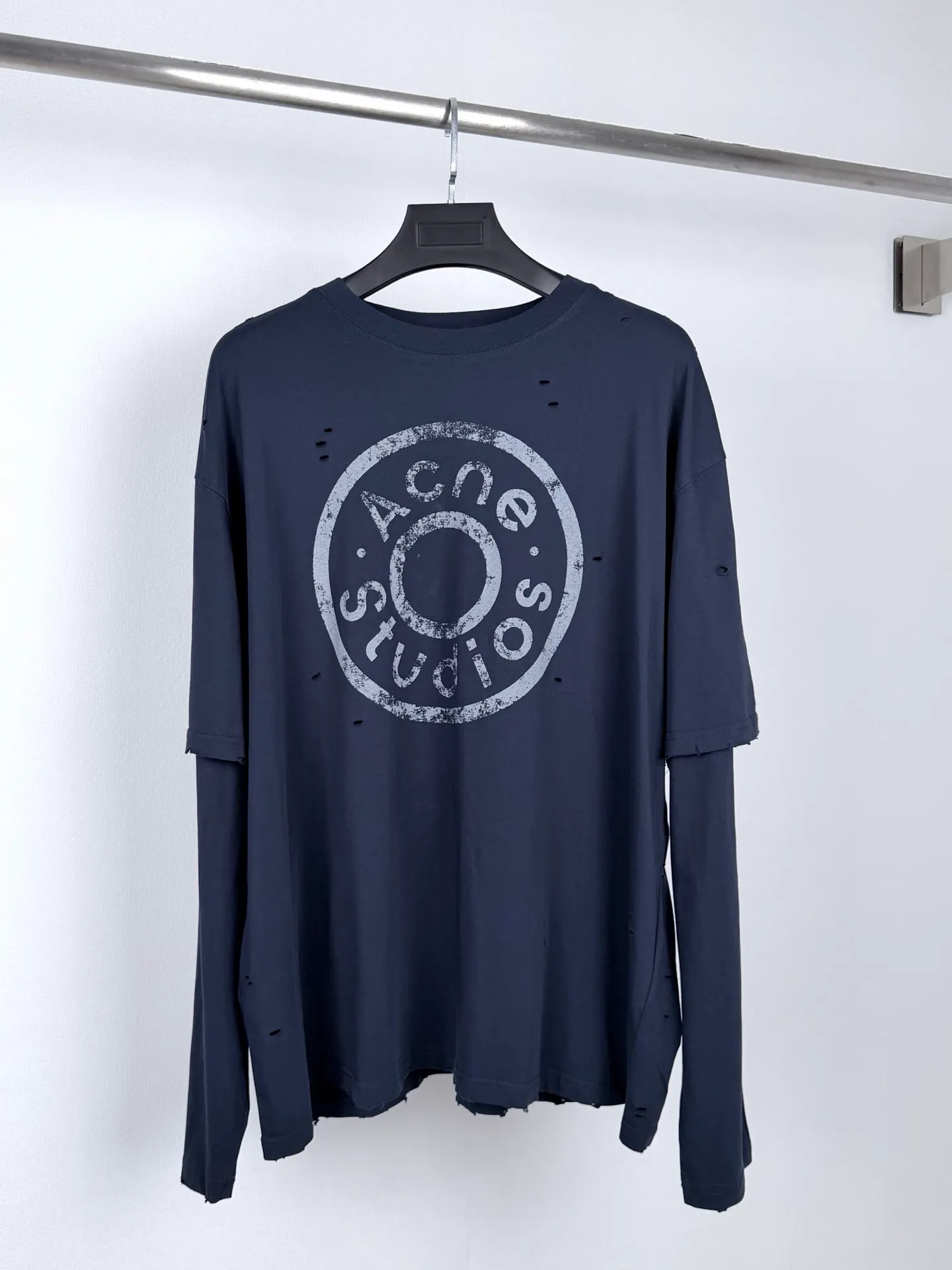 Acne Studios fake two-piece long-sleeved T-shirt with distressed logo. Customized Arashi weft-order plain cotton. Delicate and soft, warm and skin-friendly. Indigo-green covering the body. Matt low-saturation tones. Spreading the unique cool and relaxed charm of Retro deconstruction. The neat round neck is simple and restrained. The layered structure skillfully creates fake two-piece layers. The three-dimensional look of short sleeves stacked on long sleeves is naturally revealed in silence. The chest is embellished with the seasonal denim-style rivet logo. The Retro imprint is dimly deposited on the fabric. The body is staggered with frayed holes and stretches casually. The original texture of the deconstructed fabric. The loose shoulder silhouette is relaxed and relaxed. The cool and deconstructed Nordic aesthetics are integrated into daily clothing. The avant-garde quiet luxury style of alienation and restraint is demonstrated. Process 1: Using glue printing. The chest printing has been revised three times with the film screen. Use glue liquid paint to print the pattern on the fabric. Bake the fabric to fix the printing pattern. Process 2: Many parts of the body of the garment are worn by pure artificial regular positioning and manual brushing to add texture and depth to the surface of the garment to imitate the texture of natural wear and tear. Process 3: The fabrics are fermented and washed to give a better hand feel. Not easy to deform, not easy to shrink, not easy to fade, and maintain long-term beauty. Accessories: Customized 1:1 Acne trademark. Fit: Loose fit. Size: S M L XL